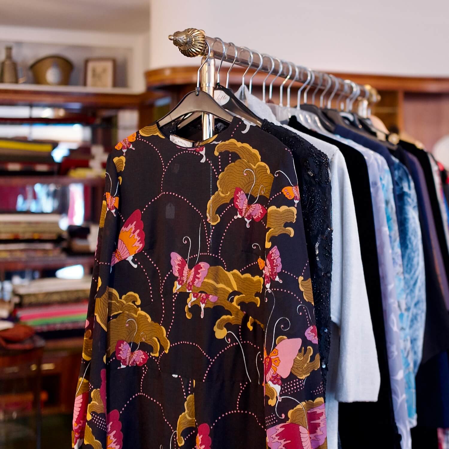 Ein Kleiderständer mit ausgewählter Secondhand-Kleidung, darunter eine wunderschöne Bluse mit Schmetterlingsmuster bei Aventures de Paulette in Hamburg, entdecke nachhaltige und einzigartige Fashion.