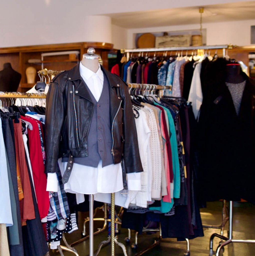Eine faszinierende Innenansicht von Aventures de Paulette in Hamburg, mit einer Vielzahl von Kleiderständern, die Blusen, Röcke, Hosen, Kleider, Mäntel und eine schwarze Lederjacke präsentieren, finde deinen individuellen Stil.