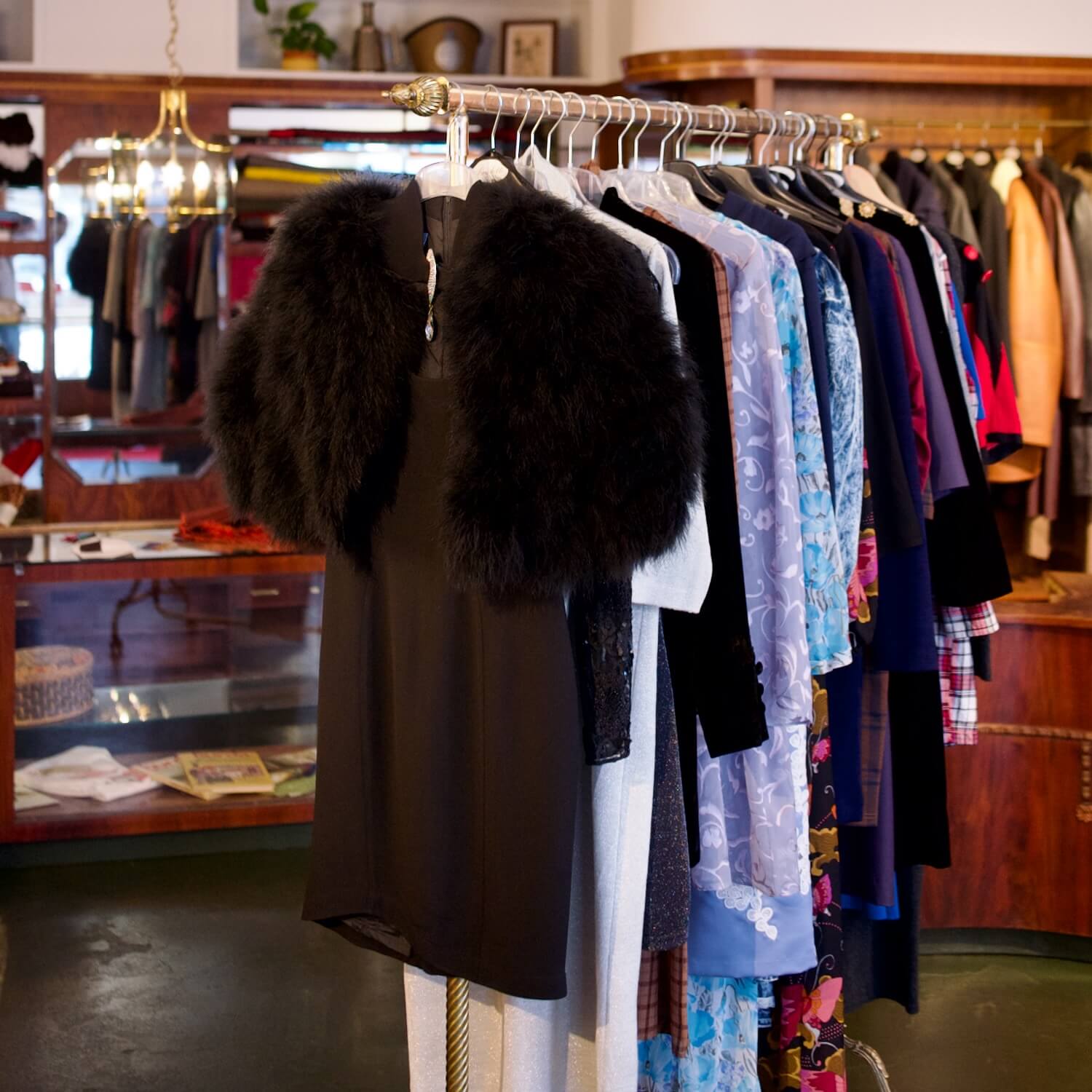 Eine Innenansicht von Aventures de Paulette in Hamburg, mit einem Kleiderständer voller Vintagekleidung und einem wunderschönen Kleid mit Pelzbesatz, entdecke einzigartige Vintage-Fashion.